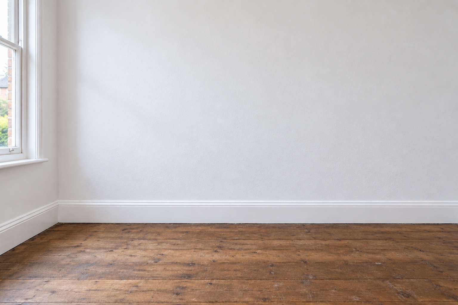 The same UK interior wall freshly plastered and painted, with clean white skirting